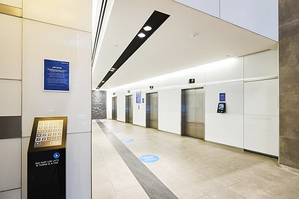 modern-office-elevator-lobby-kiosk Modern office elevator lobby with multiple elevator doors, floor direction markers, and a self-service kiosk near the entrance.